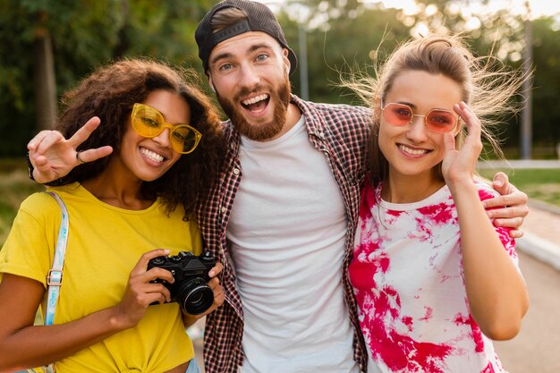 一緒に楽しんでいる写真カメラ、男性と女性と一緒に公園を歩いている感情的な笑顔の友人の幸せな若い会社