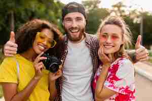 Free photo happy young company of emotional smiling friends walking in park with photo camera, man and women having fun together