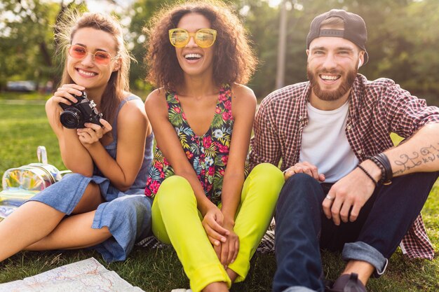 Happy young company of friends sitting park, man and women having fun together, traveling with camera,