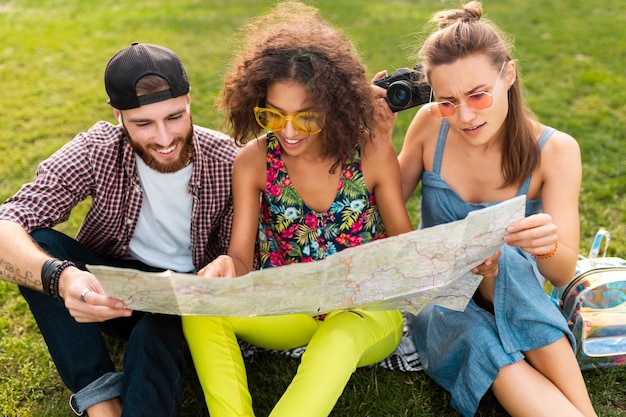 Felice giovane compagnia di amici seduti nel parco che viaggiano guardando nella mappa visite turistiche, uomini e donne che si divertono insieme