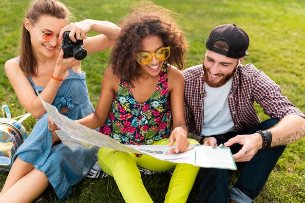 Happy young company of friends sitting park traveling looking in map sightseeing, man and women having fun together