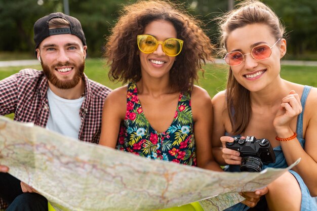 Happy young company of friends sitting park traveling looking in map sightseeing, man and women having fun together