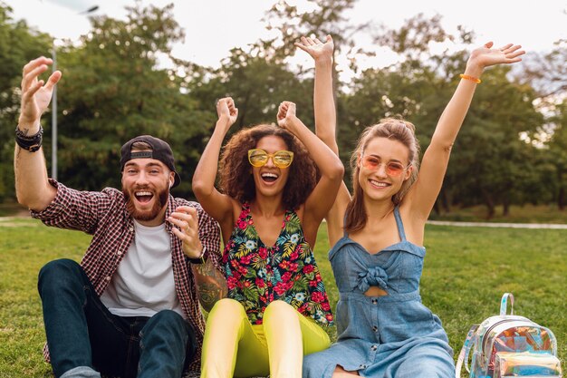 Happy young company of smiling friends sitting park on grass, man and women having fun together