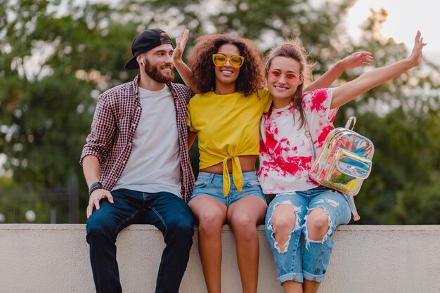 Happy young company of smiling friends sitting in park, man and women having fun together