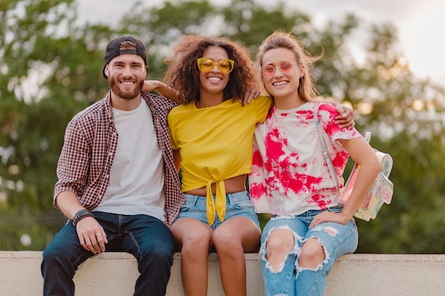 Happy young company of smiling friends sitting in park, man and women having fun together