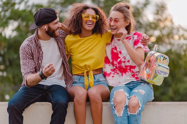 Happy young company of smiling friends sitting in park, man and women having fun together