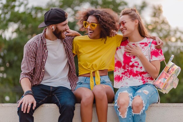 Happy young company of smiling friends sitting in park, man and women having fun together