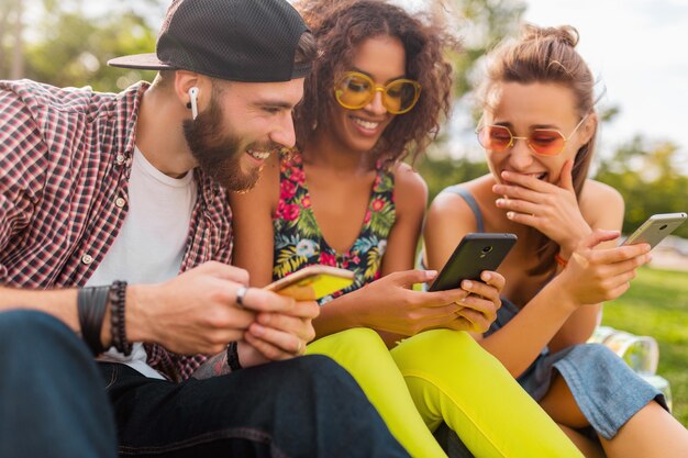スマートフォンを使って公園に座っている笑顔の友達、一緒に楽しんでいる男性と女性の幸せな若い会社