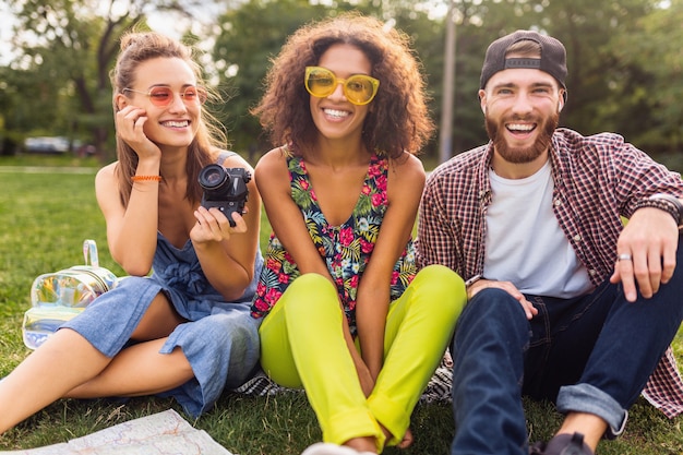 Felice giovane compagnia di parlare sorridenti amici seduti nel parco, uomo e donna che si divertono insieme, viaggiando con la macchina fotografica