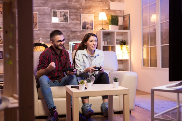 Счастливая молодая пара после победы в видеоиграх на телевидении, сидя на диване ночью.