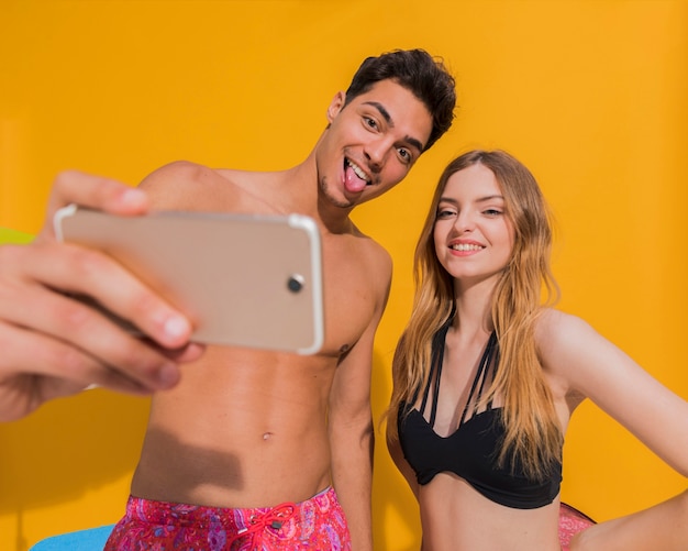 Happy young couple in beachwear making selfie on smartphone in studio