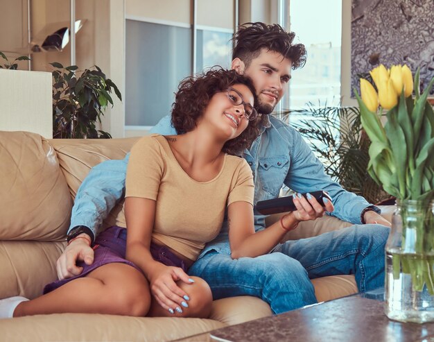 Happy young couple cuddling while watching TV in their living room.