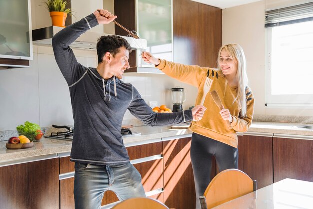 Happy young couple fighting with spatula and whisk