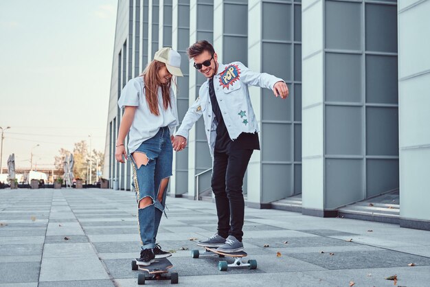 現代の通りでスケートボードを運転しながら楽しんで幸せな若いカップル。
