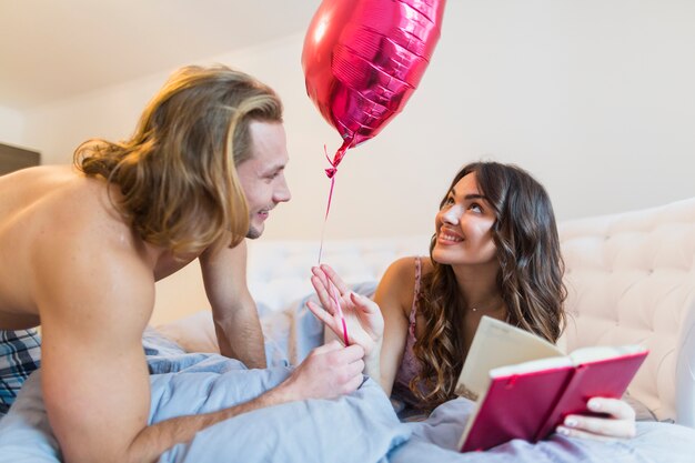 Счастливая молодая пара держит в руках розовый воздушный шар в форме сердца