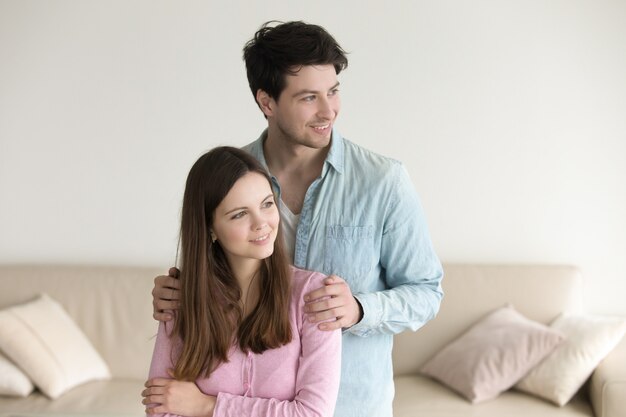 Happy young couple at home, standing together, smiling, looking