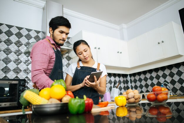 Happy young couple is using digital tablet for looking method of cooking 