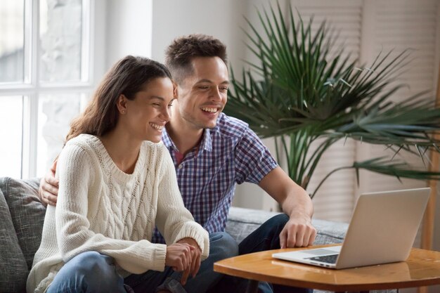 Happy young couple laughing watching funny video or making videocall