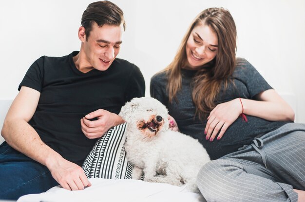 Happy young couple looking at friendly toy poodle sitting on bed