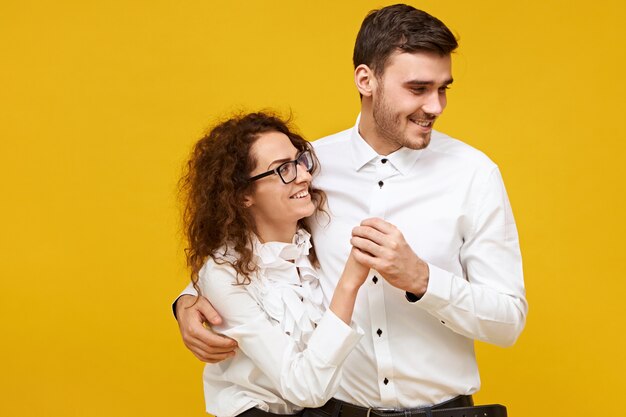 Happy young couple in love enjoying nice time together on first date. Attractive man and woman dancing, having joyful looks, wearing white shirts. Togetherness, family and relationships concept