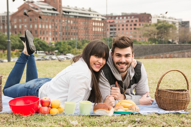 Happy young couple lying on blanket with many healthy snack in picnic