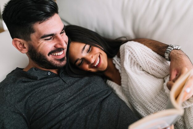 Happy young couple lying on sofa reading book