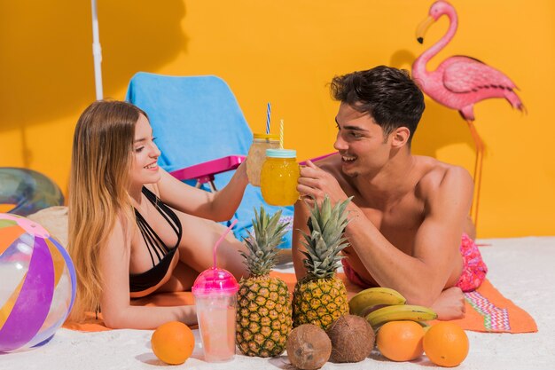Happy young couple lying with cocktails on beach in studio