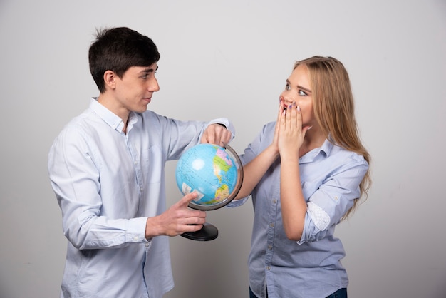 Free photo happy young couple planning their anniversary destination holding up a globe.