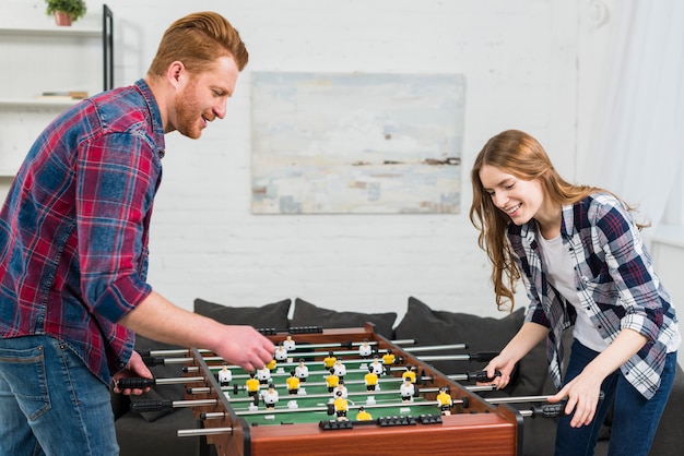 Foto gratuita giovani coppie felici che giocano il gioco di calcio della tavola di calcio a casa