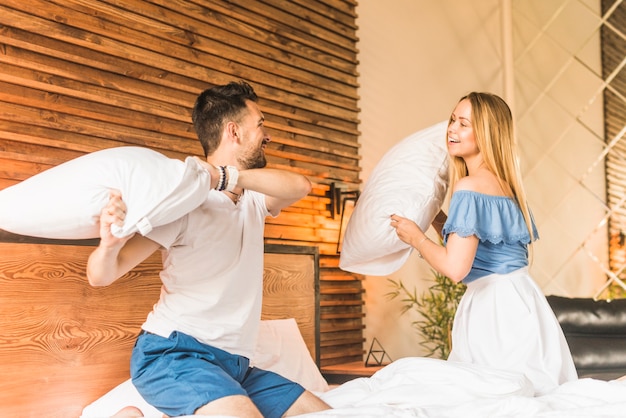 Free photo happy young couple playing with pillows on bed