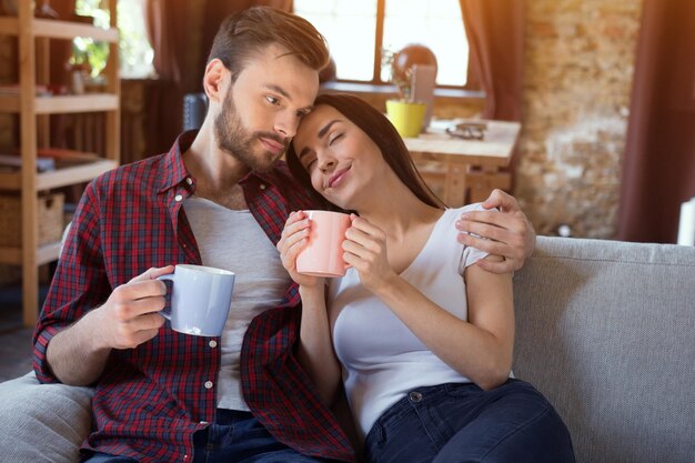 幸せな若いカップルは、屋内のモダンな家のリビングルームでリラックスします。恋するカップル-ラブストーリーの始まり