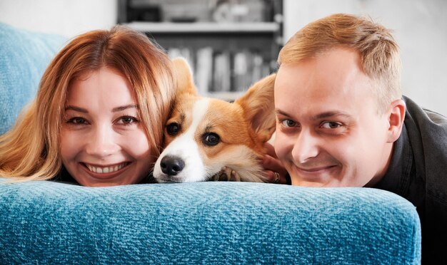 Счастливая молодая пара отдыхает на диване с милой собакой Корги