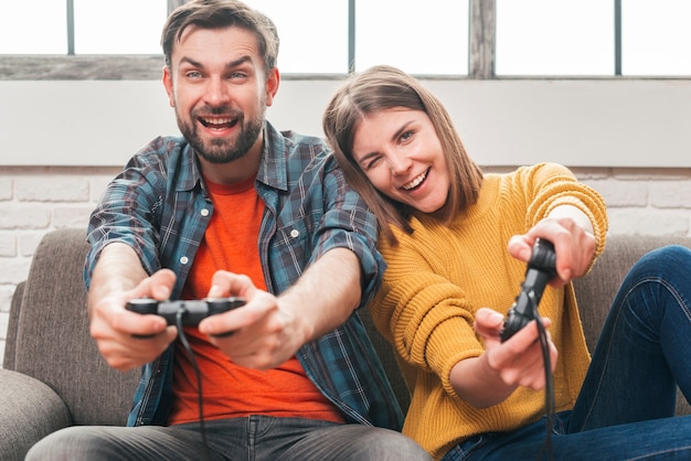 ビデオゲームをプレイしながら楽しんでソファーに座っていた幸せな若いカップル