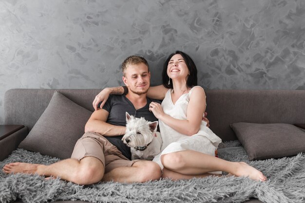 Счастливая молодая пара, сидя на диване с белой собакой