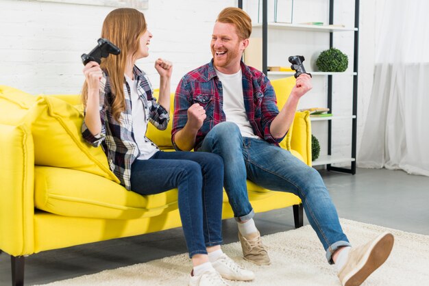 Happy young couple sitting on yellow sofa clenching their fist like winner after playing the video game