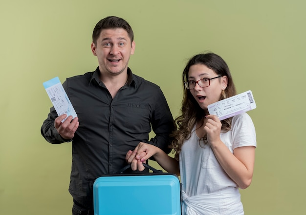 Free photo happy young couple of tourists man and woman holding air tickets and suitcase over light