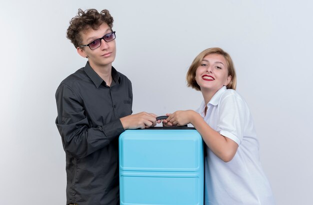 Happy young couple of tourists man and woman holding suitcase  smiling over white wall