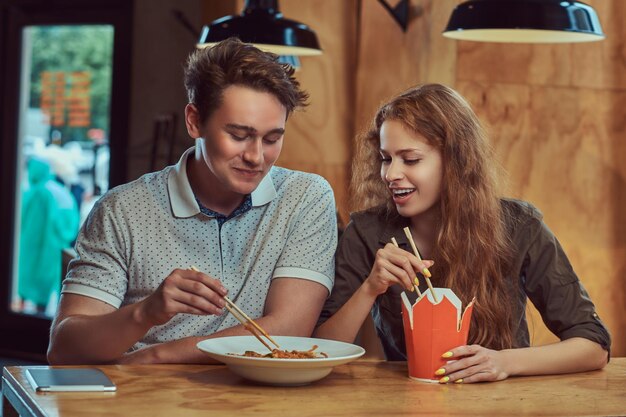 Happy young couple wearing casual clothes eating spicy noodles in an Asian restaurant.