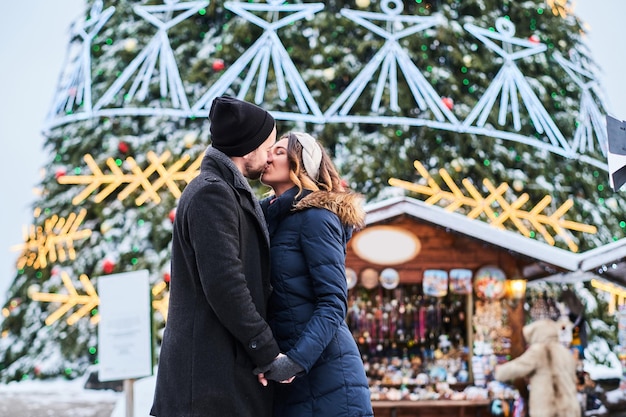 Happy young couple wearing warm clothes standing near a city Christmas tree, enjoying spending time together