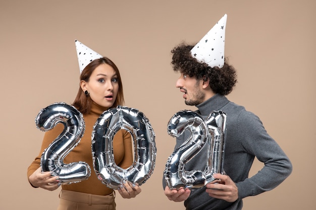 Happy young couple with confused facial expression wear new year hat poses for camera Girl