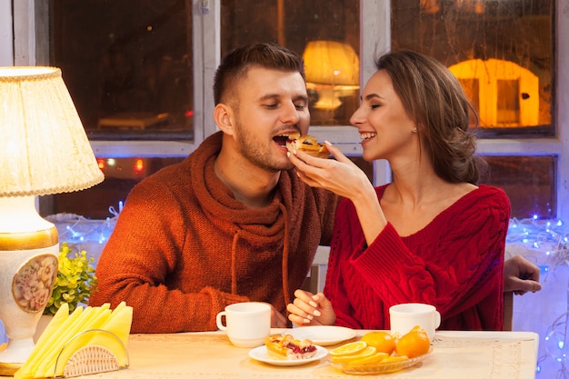 The happy young couple with cups of tea and cakes.