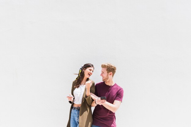 Happy young couple with smartphone standing against white background