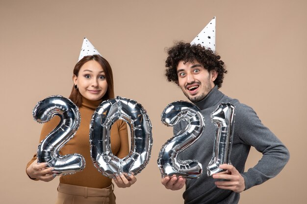 Happy young couple with surprised facial expression with new year hat poses for camera Girl showing and and guy with and on gray