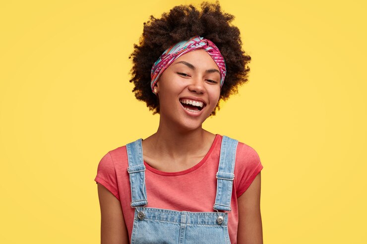 Free Photo happy young dark skinned female with afro hairstyle, dressed in casual outfit, rejoices finishing household duties, has toothy smile, isolated over yellow wall. positive emotions concept
