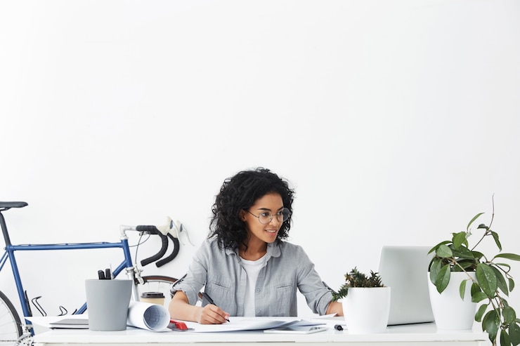 Free Photo happy young dark-skinned woman architect wearing round eyeglasses and grey shirt smiling