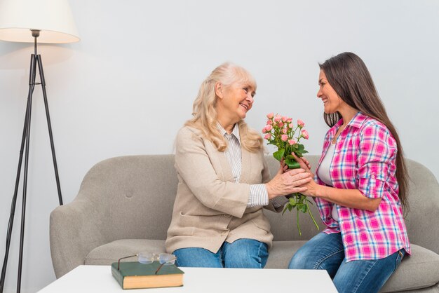 Happy young daughter giving senior mother flower bouquet