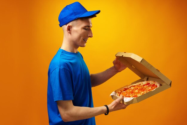 Happy young delivery man holding pizza box against yellow background