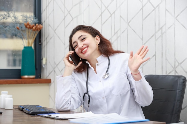 幸せな若い医者はオフィスに座って電話で話している高品質の写真