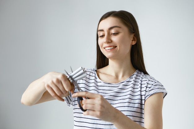 Happy young European woman feeling free of destructive unhealthy tobacco addiction, holding several cigarette and cutting them in halves using scissors