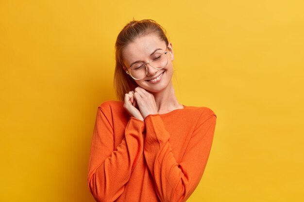 Happy young European woman with pleased expression closes eyes and smiles gently tilting her head